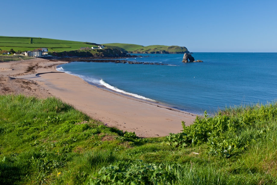 Sandy beach and turquoise sea at Thurlestone with green cliffs and iconic rock arch