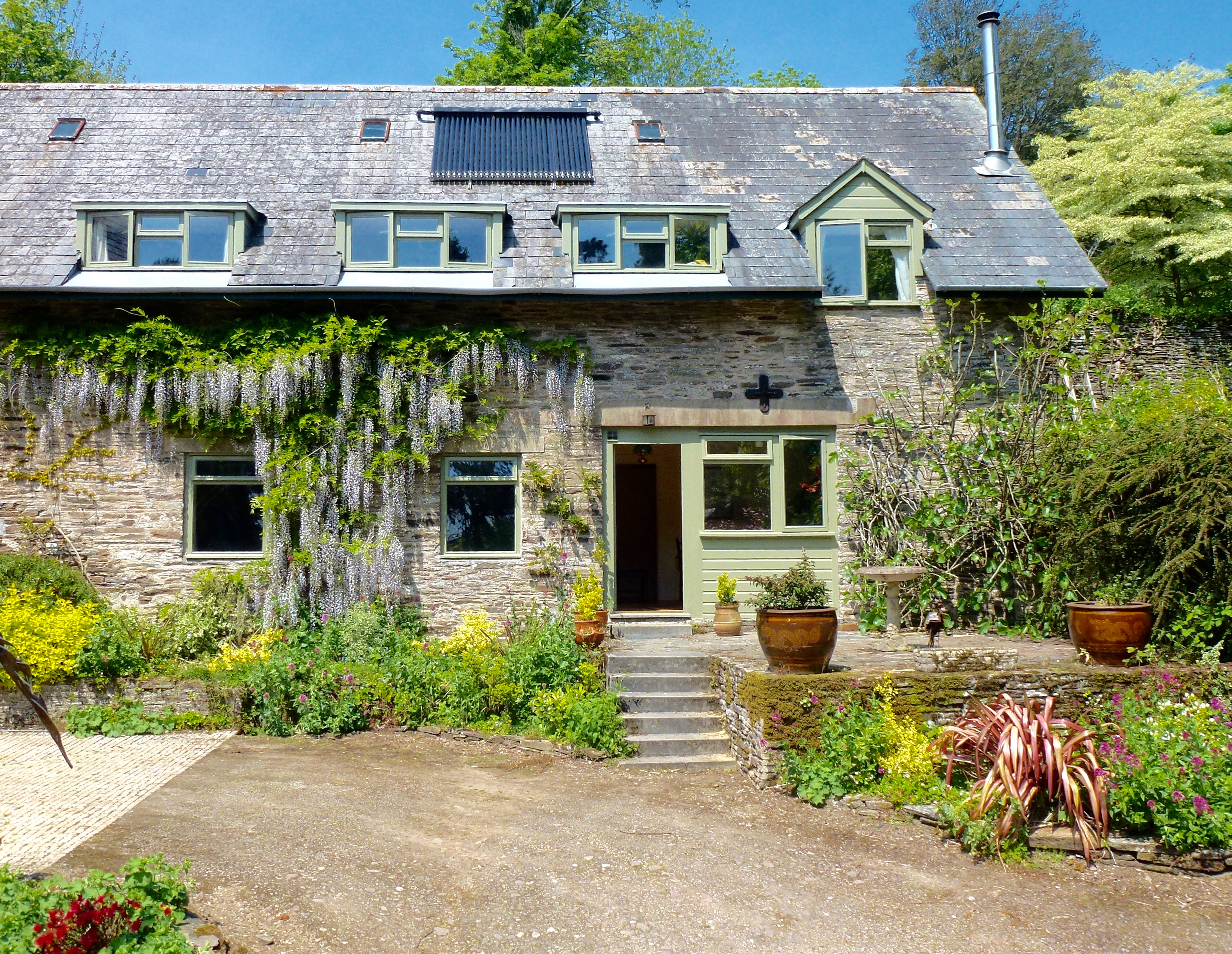 Stone Coach House entrance with wisteria, slate roof, dormer windows, and planted courtyard