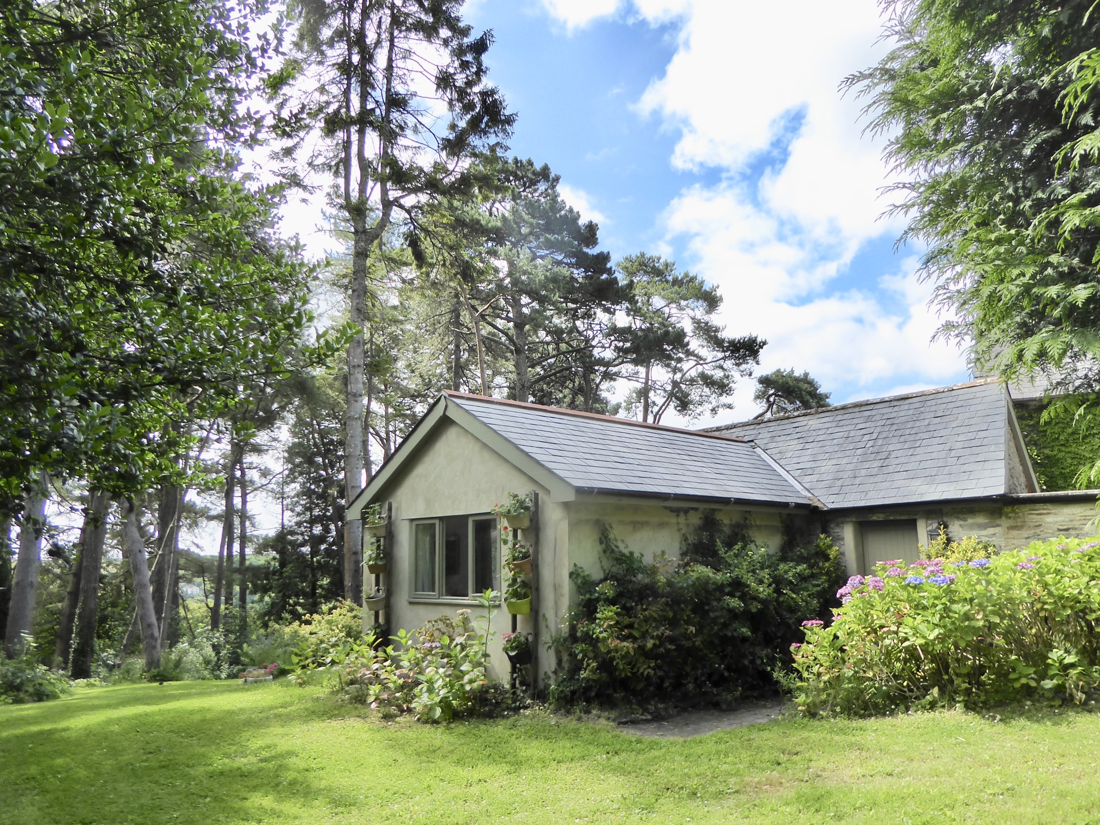 Charming single-storey cottage surrounded by tall pines, hydrangeas, and a manicured lawn