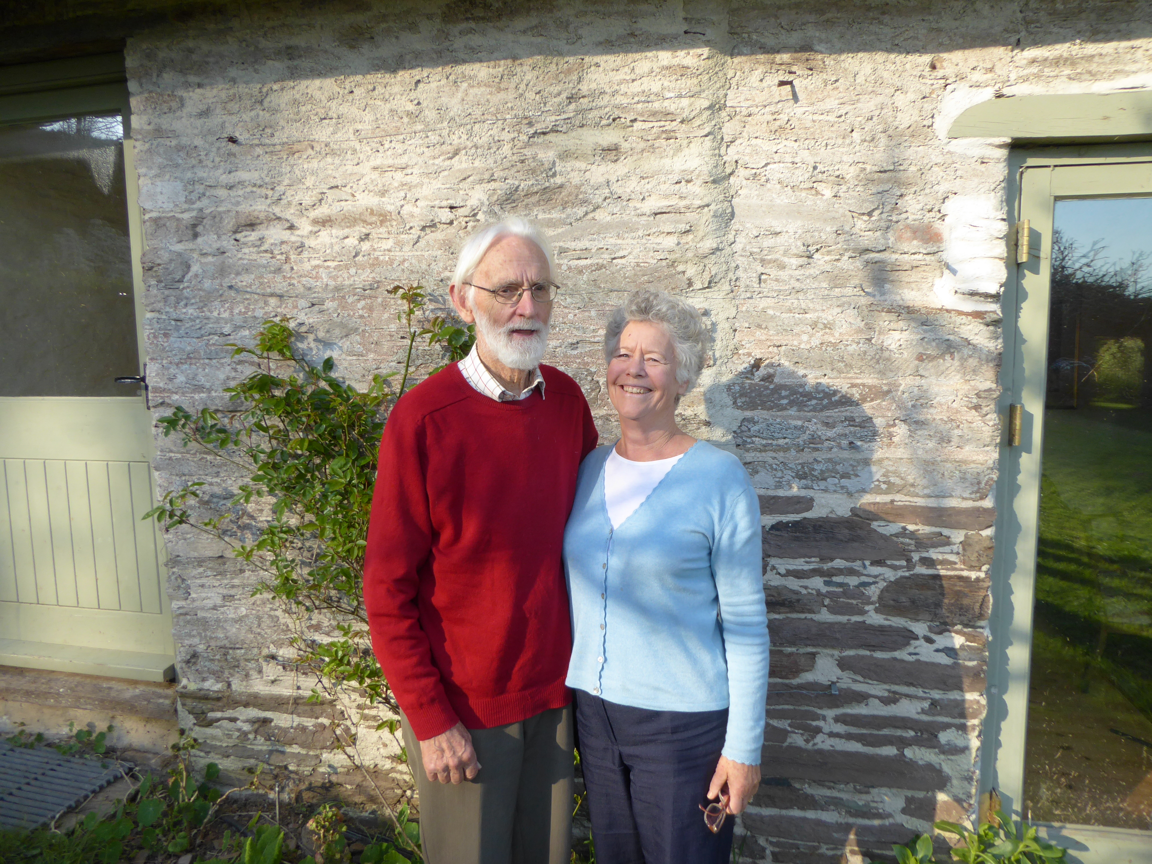 Johnny and Rosalind, your hosts, standing outside the stone property on a sunny day